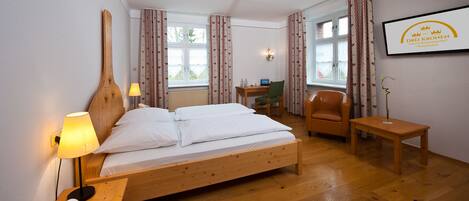 A hotel room with a wooden bed, a desk with a computer, a chair, and a small table.
