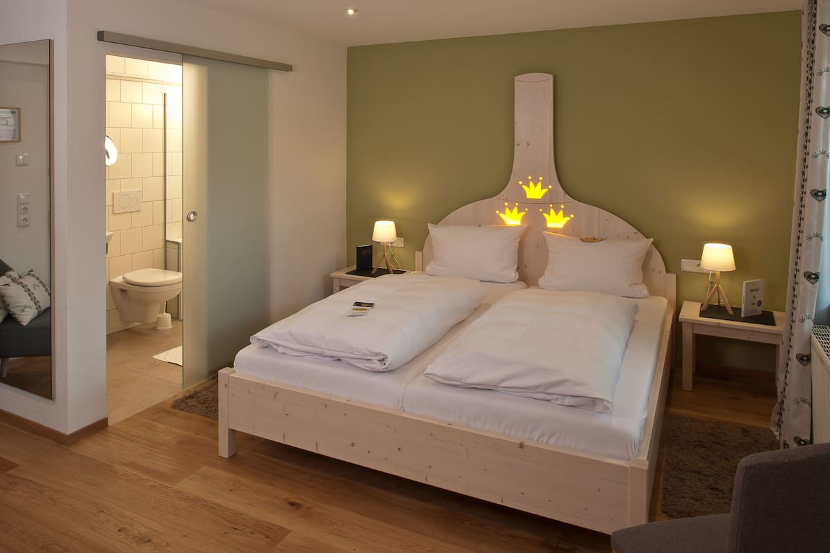 A double bed with a wooden headboard, two bedside tables with lamps, a bathroom visible through an open door, and a mirror on the left wall.