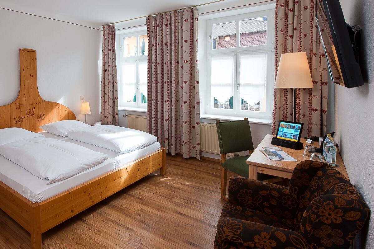 A hotel room with a wooden bed, two bedside tables with lamps, a desk with a computer, and a chair.