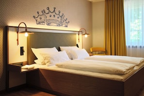 A hotel room with a large bed, two bedside lamps, a nightstand, a chair, and a crown design on the wall. - Hotel & Brauereigasthof Drei Kronen (Memmelsdorf)