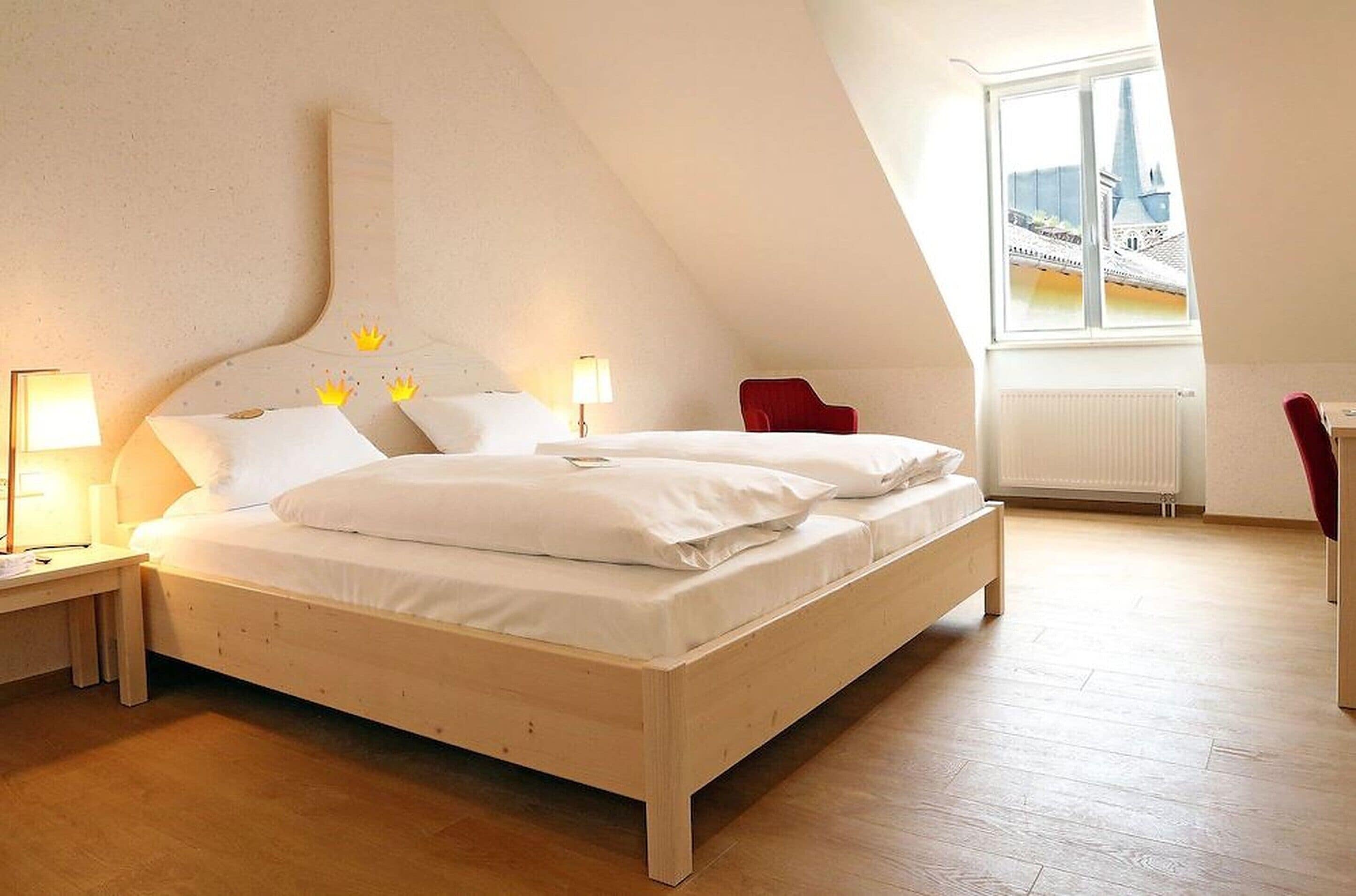 A bedroom with a wooden bed, two bedside tables with lamps, a red chair, and a window with a view of buildings.
