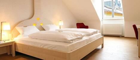 A bedroom with a wooden bed, two bedside tables with lamps, a red chair, and a window with a view of buildings.