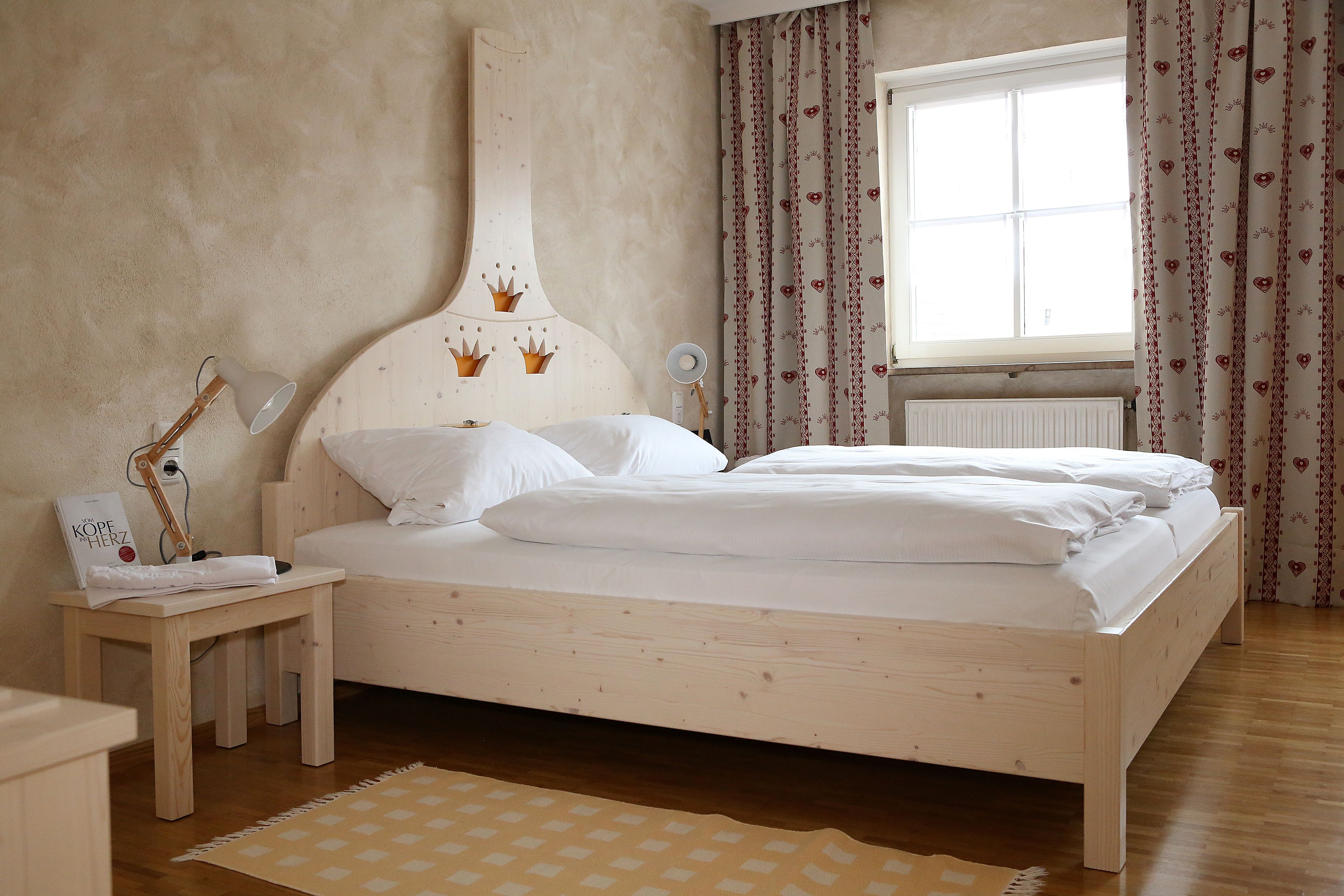 Un dormitorio con una cama de madera, una mesita de noche con lámpara, una mesita auxiliar y una ventana con cortinas.
