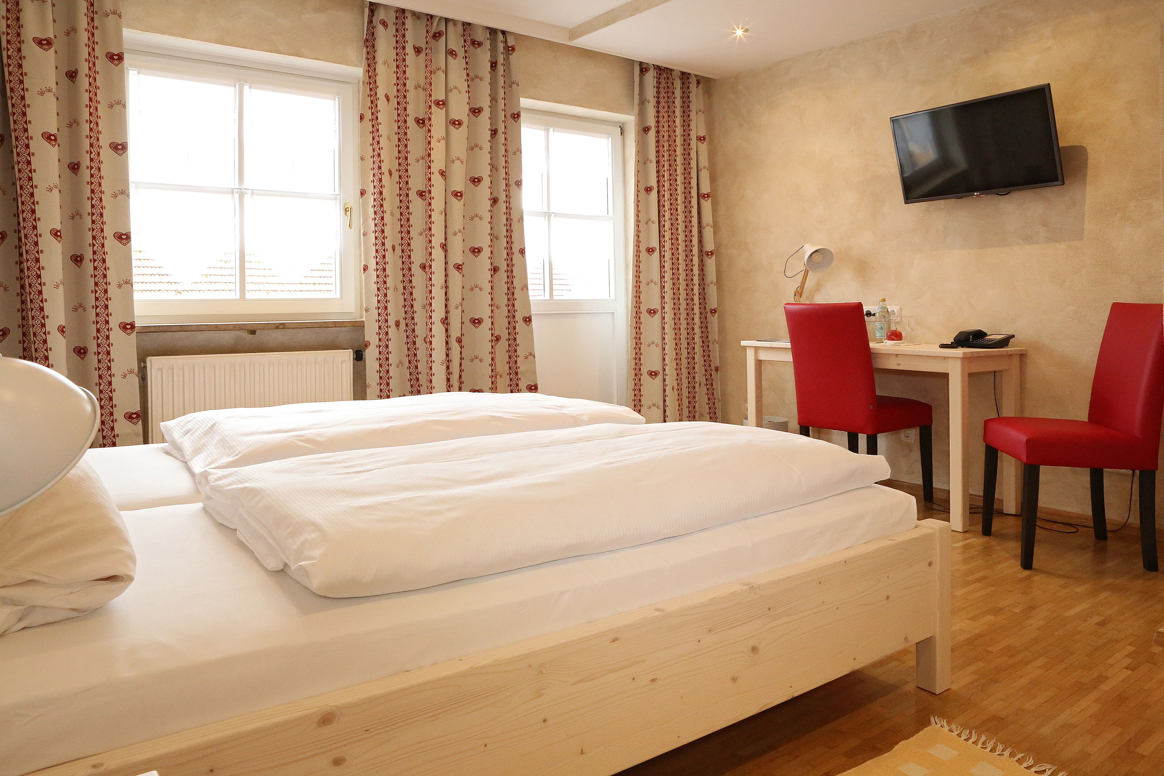 Ein Hotelzimmer mit einem Bett, einem Schreibtisch, zwei roten Sesseln, einem Fernseher und einem Fenster mit Vorhängen.