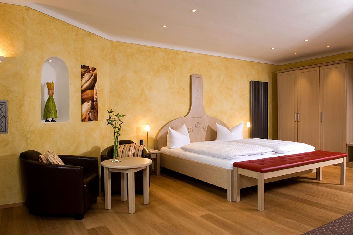 A hotel room with a large bed, a small table, a chair, and a wardrobe.