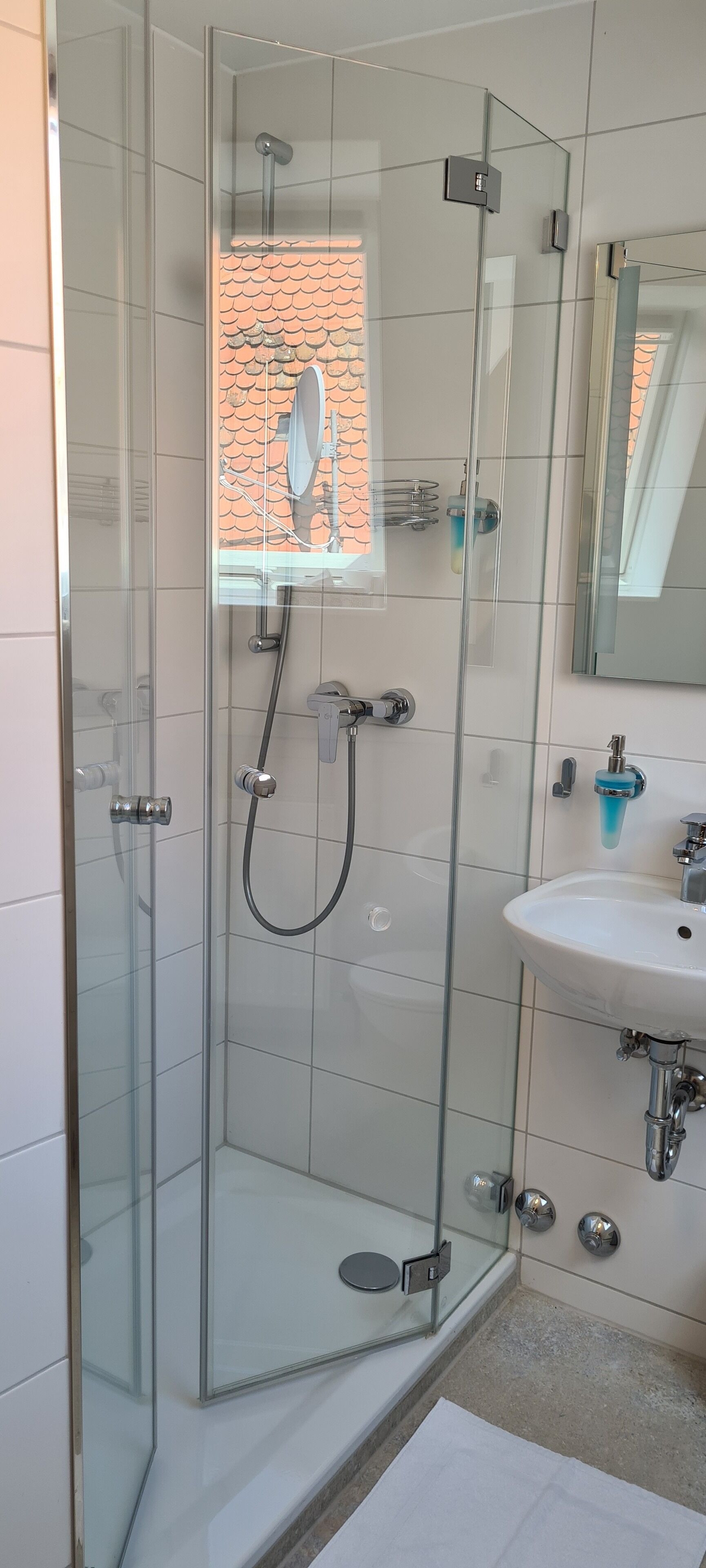 Un baño moderno con ducha envuelta en vidrio, un lavamanos blanco y un espejo.