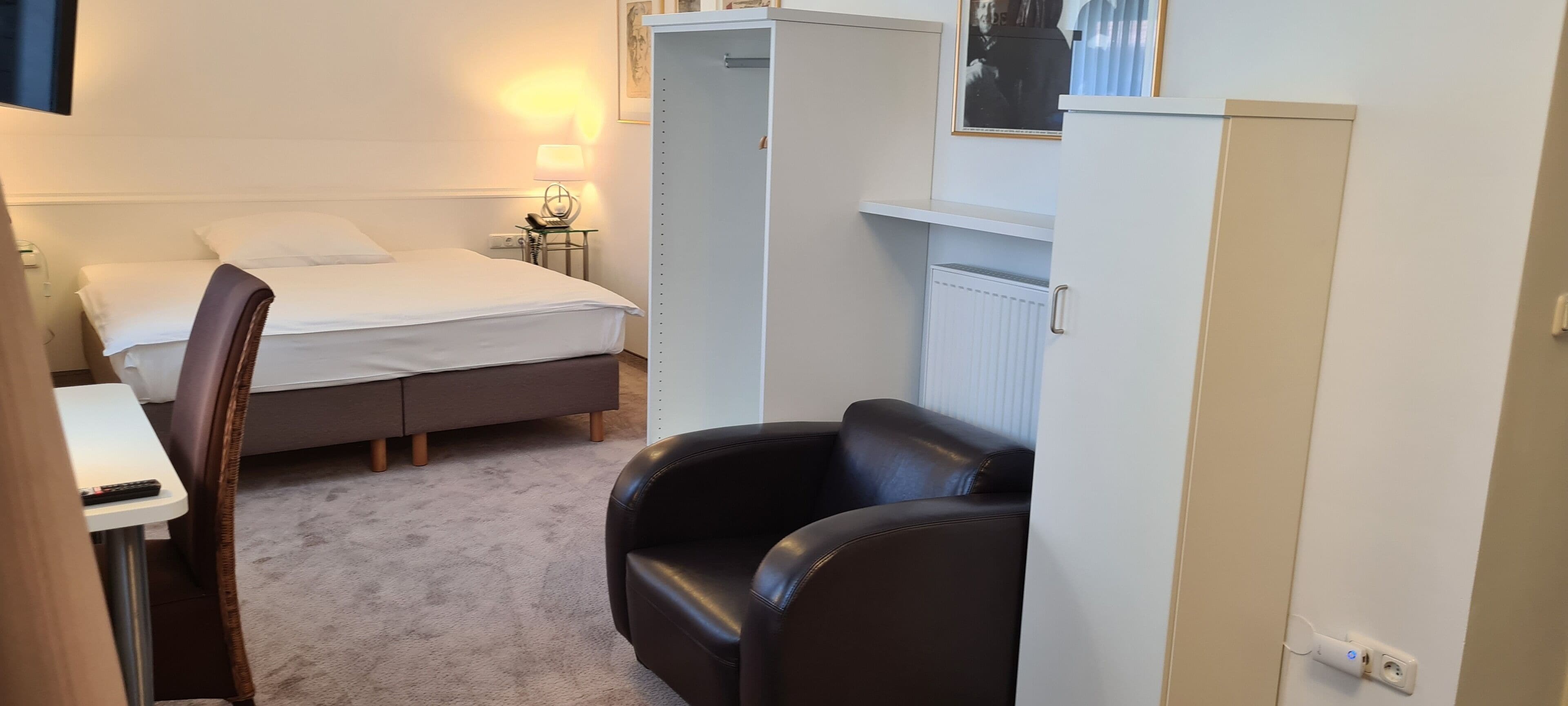 Een kleine, compacte kamer met een enkel bed, een bureau, een stoel en een kledingkast.
