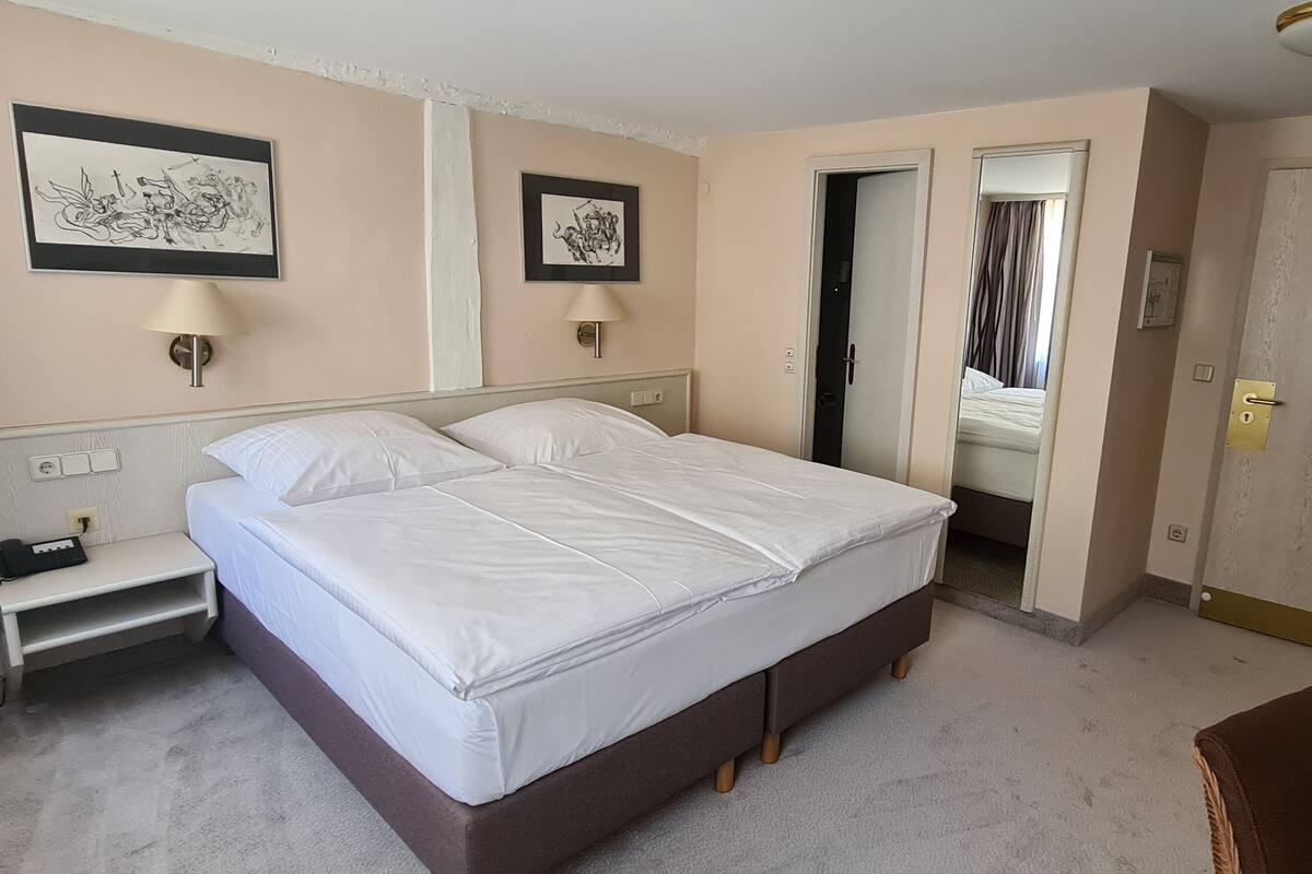 A hotel room with a large bed, bedside tables, a lamp, and a door leading to another room.