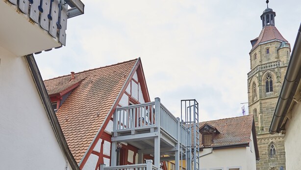 A courtyard with a balcony, white chairs, and a building with a red-tiled roof. - Hotel Garni Am Ellinger Tor (Weissenburg in Bayern)