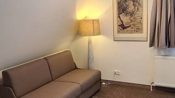 A modern living room with a brown sofa, a floor lamp, a framed artwork, and a radiator.