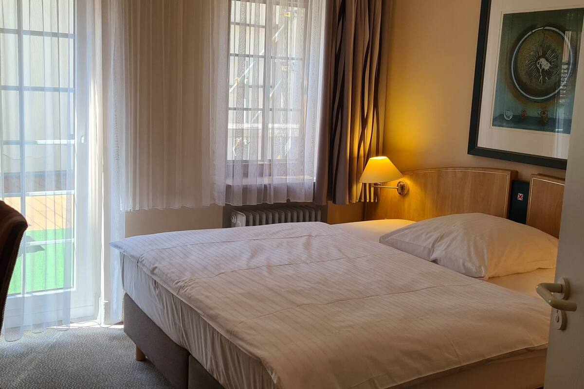 A hotel room with a bed, a desk with a computer, a lamp, and a window with curtains.