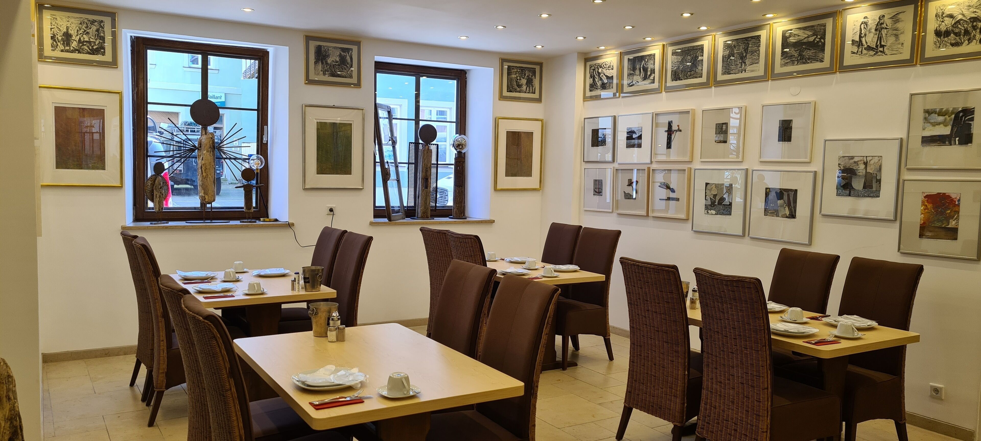Un comedor con varias mesas y sillas, obras de arte en las paredes y grandes ventanales con vistas al exterior.