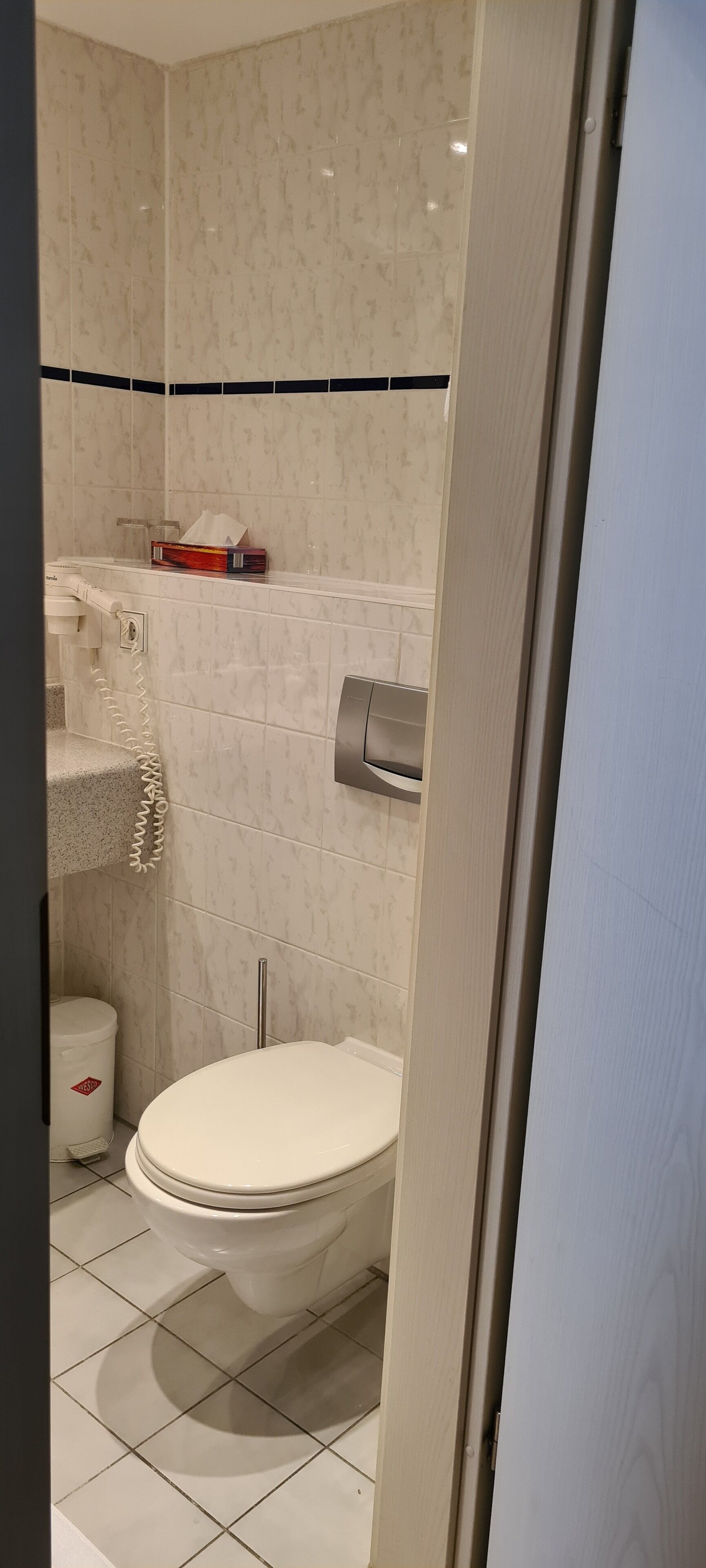 A bathroom with a toilet, a hand dryer, and a trash bin.