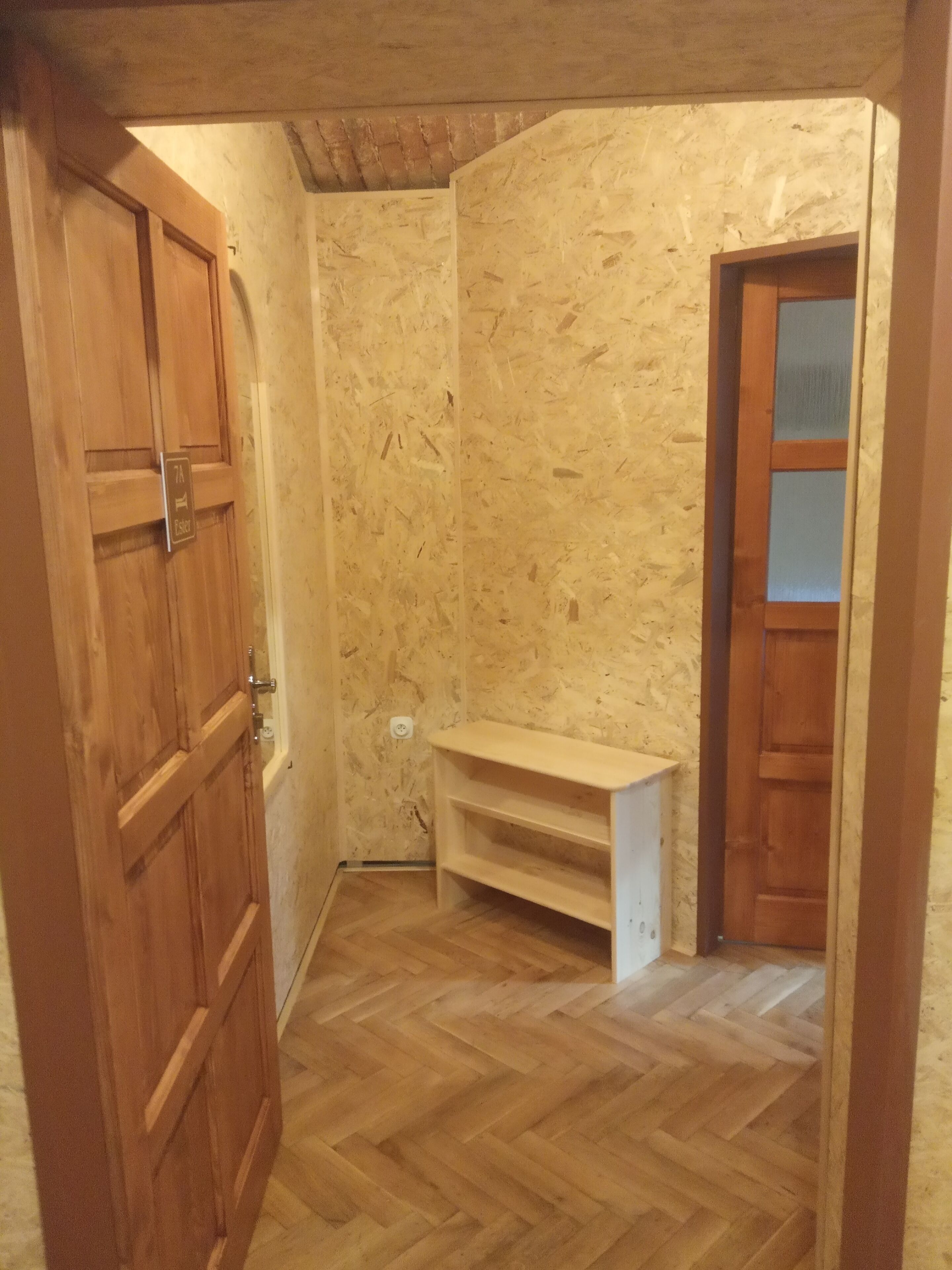 Une petite pièce fermée, dotée d’un plancher en bois, d’une banquette intégrée et d’une porte sur laquelle est apposée une pancarte.