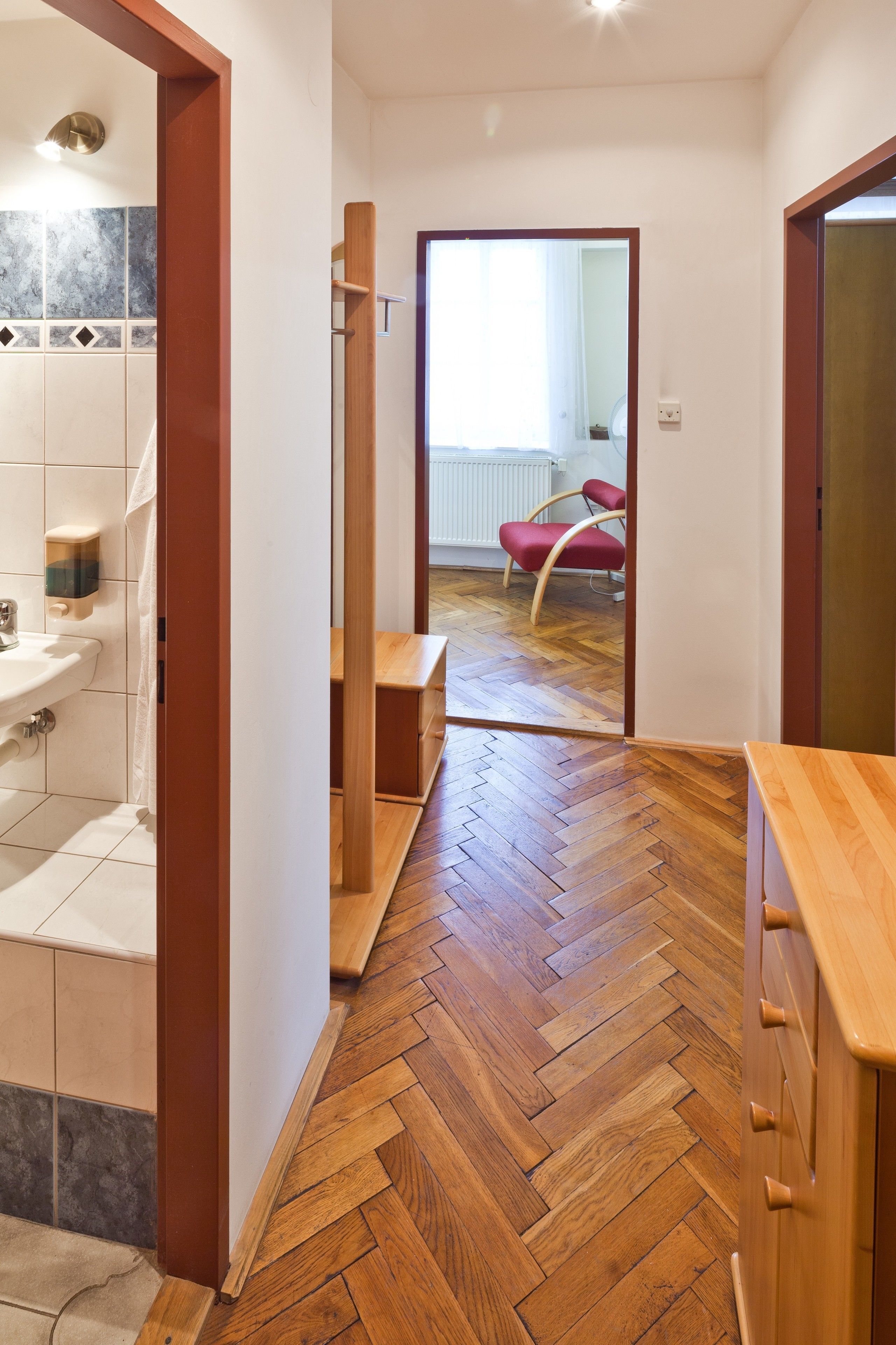 A hallway with a wooden herringbone floor, a wooden bench, and a red chair.