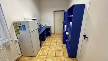 A narrow hallway with a white refrigerator, a blue counter with kitchen utensils, and a blue shelving unit with dishes.