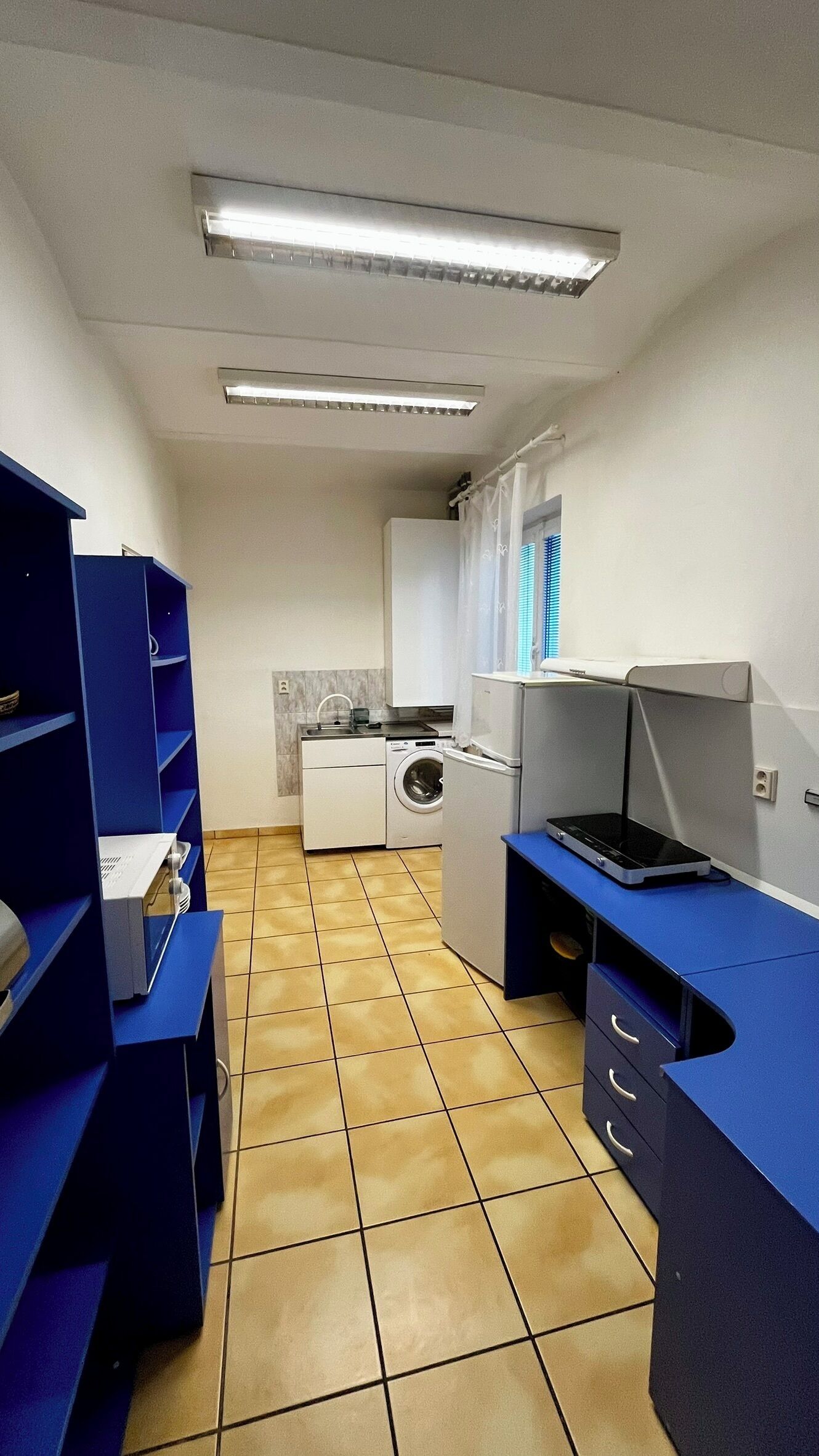 A compact kitchen with a washing machine, a refrigerator, and a blue desk area.