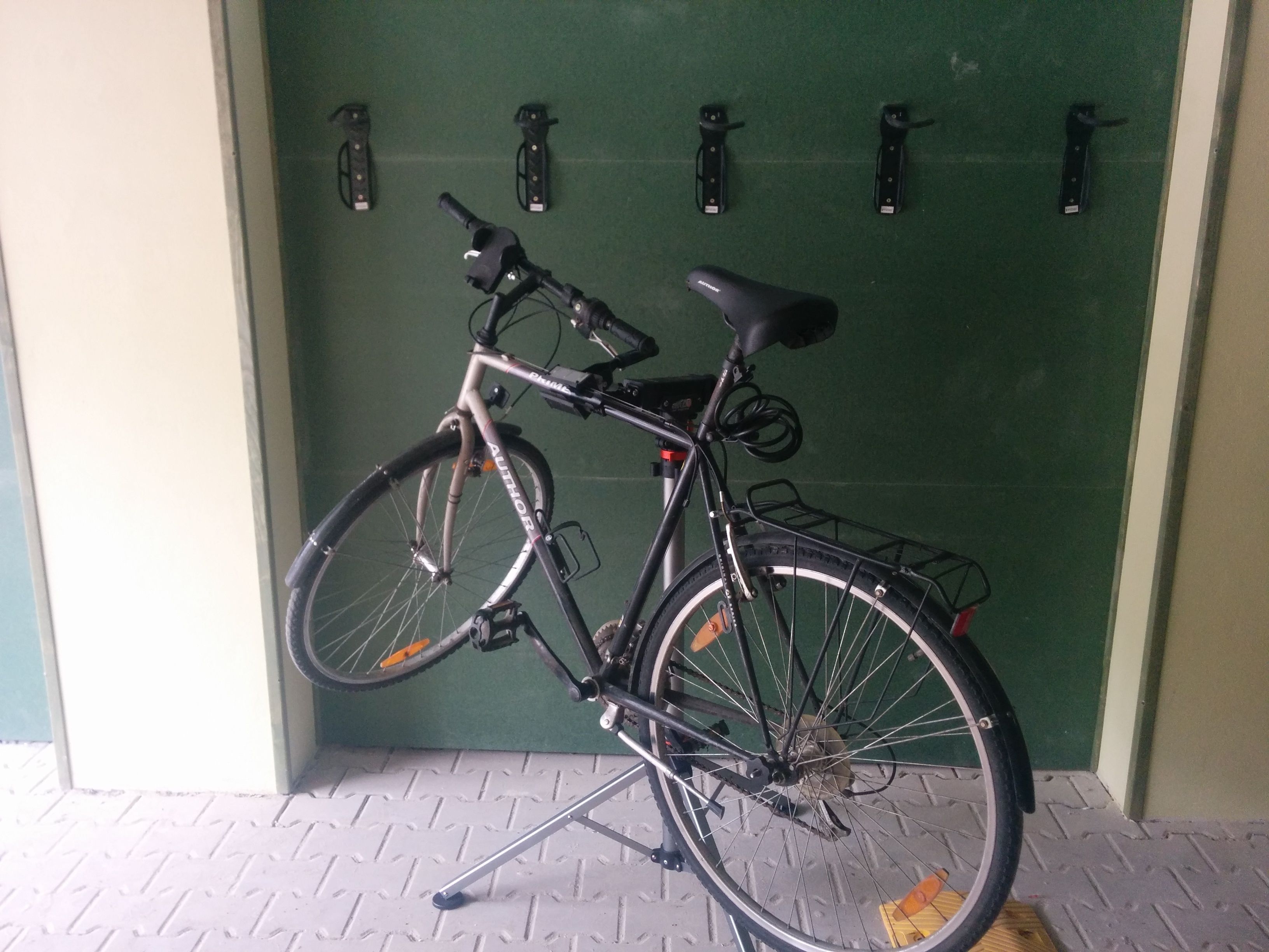 Un vélo est garé contre une porte verte, à côté d’un porte-vélo en métal.