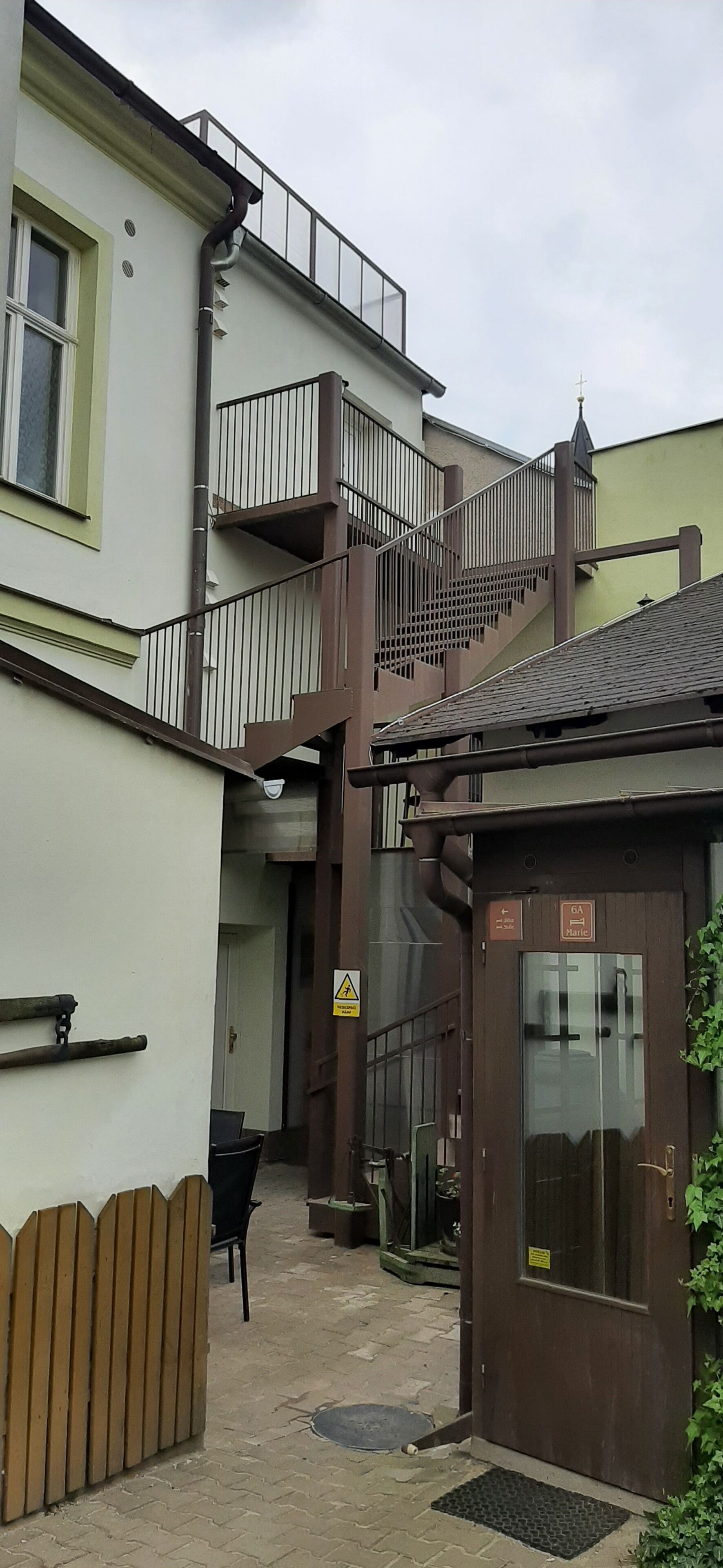 Een smalle steeg met een trap die leidt naar een balkon op de tweede verdieping. Een klein gebouw met een deur waarop 