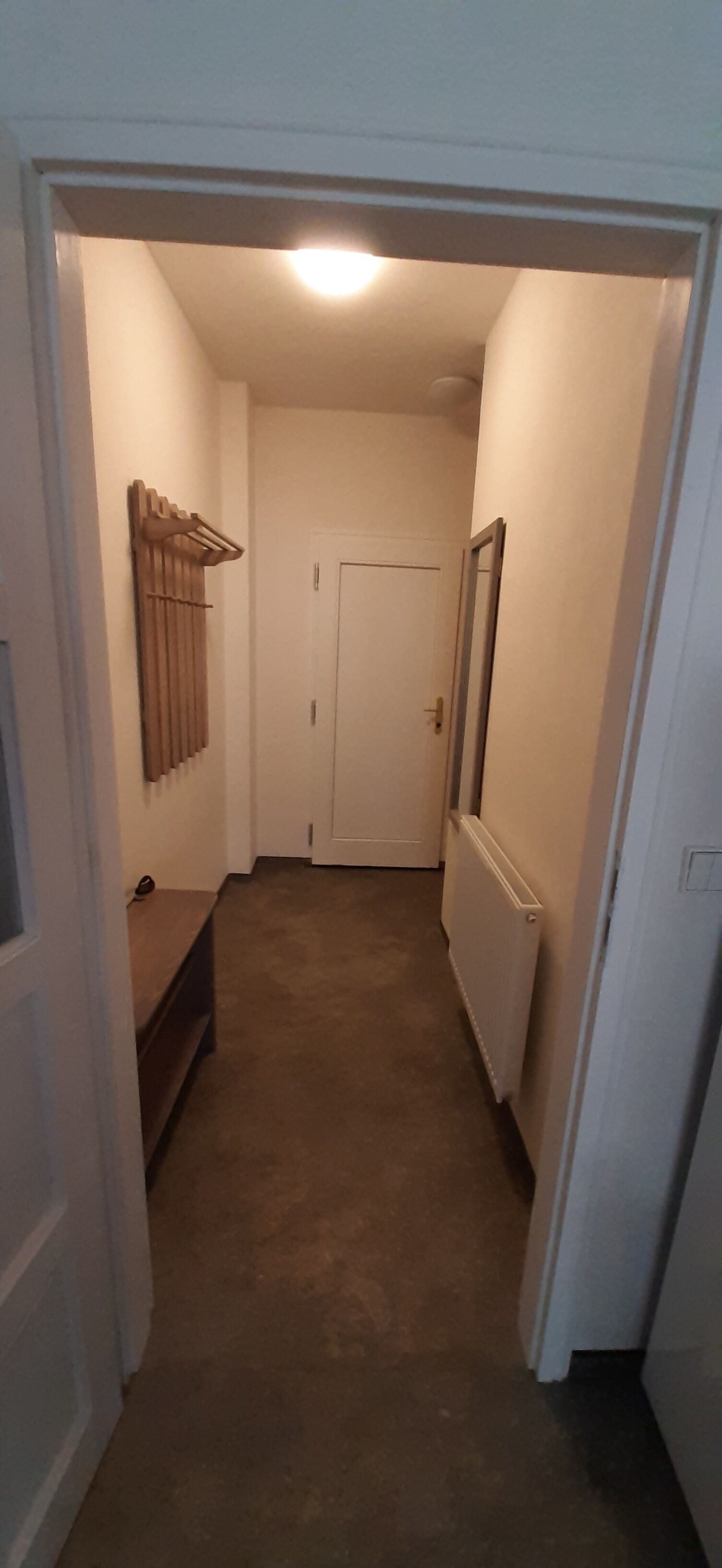 Un pasillo estrecho con un radiador, una puerta y un banco.