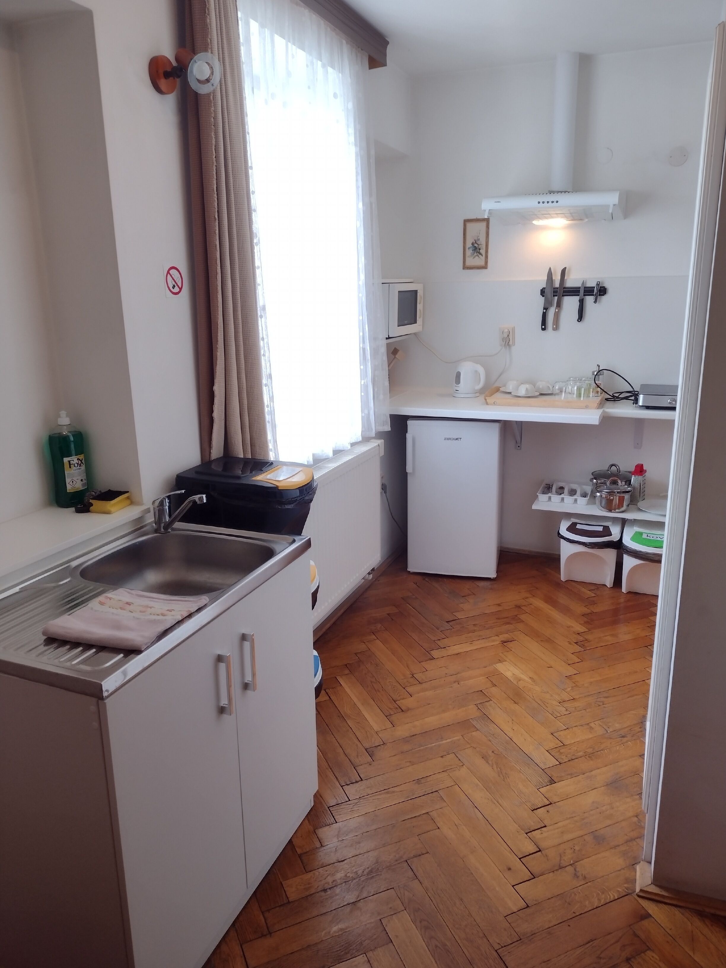 A compact kitchen with a sink, a small refrigerator, a microwave, and a kettle on the counter.