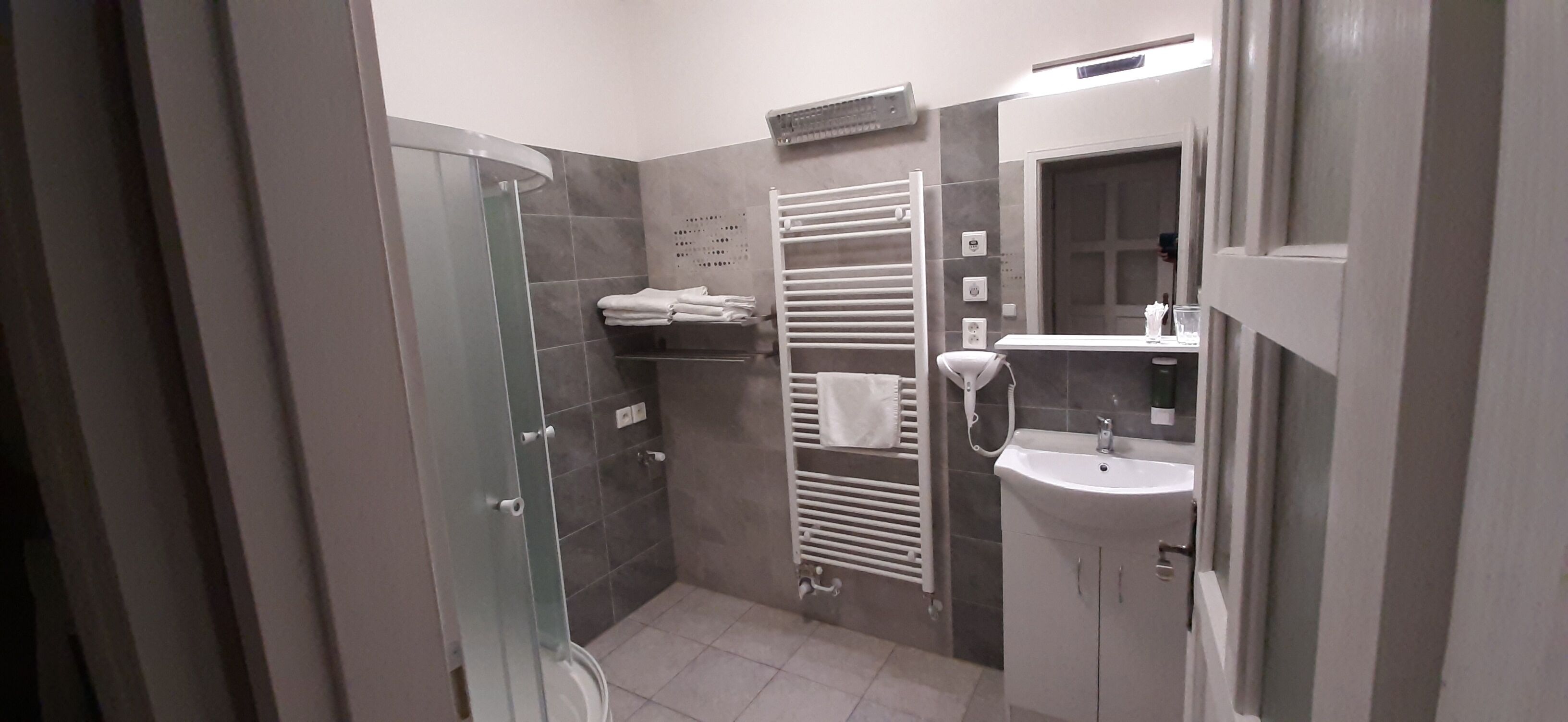 A modern bathroom with a glass shower enclosure, a white sink, and a towel rack.