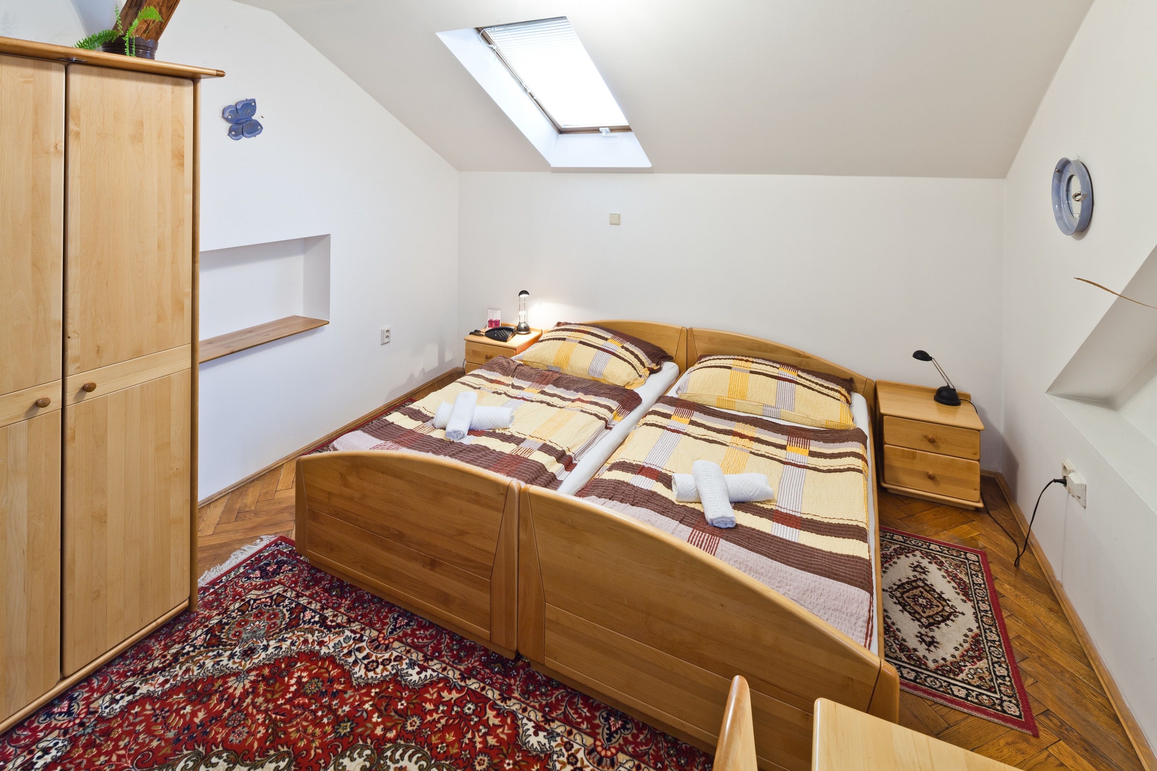 Une chambre avec un puits de lumière, un lit en bois, une table de chevet, une armoire et un tapis à motifs.