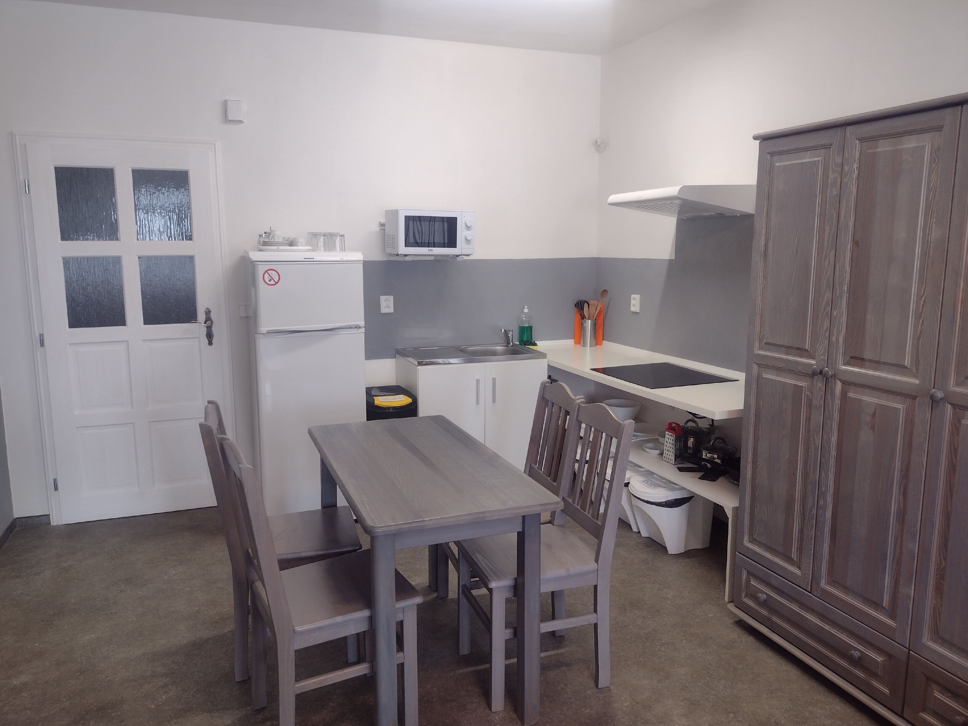 A compact kitchen with a microwave, refrigerator, and a small countertop. There is a wooden table with chairs, and a cabinet with drawers.