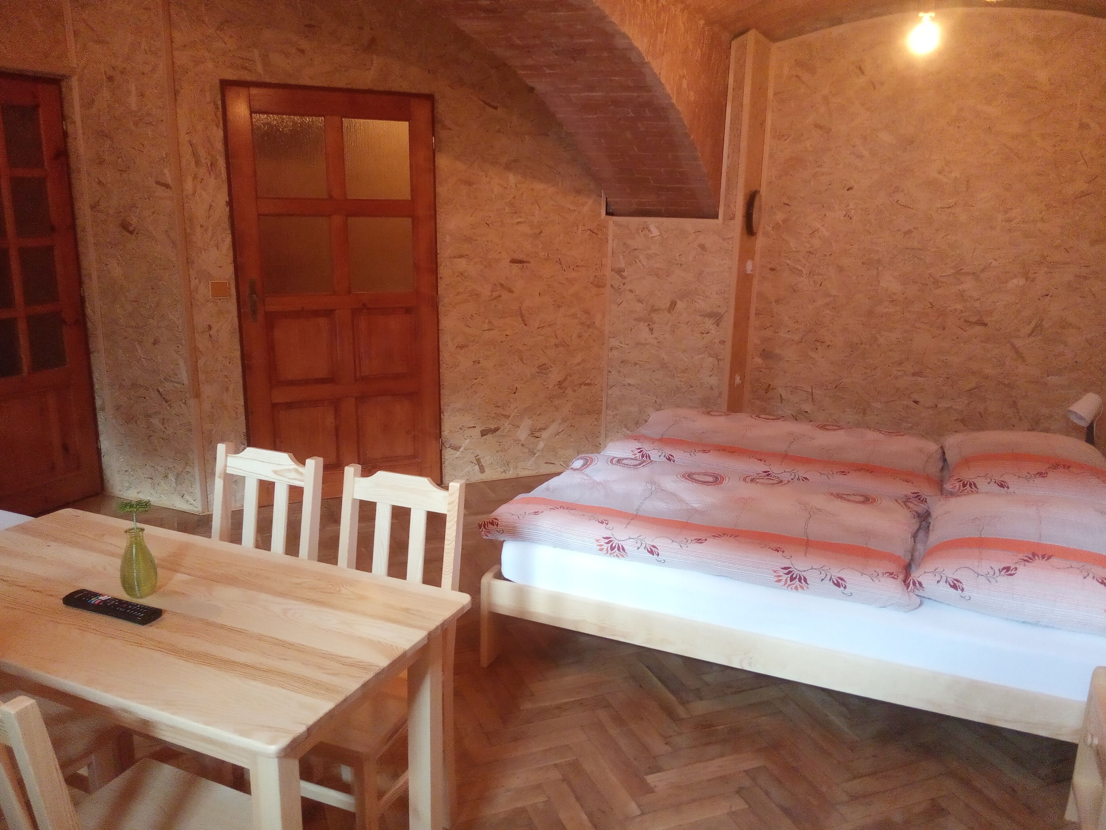 Una habitación con una mesa de madera, una silla, una cama con ropa de cama estampada y una puerta de madera.