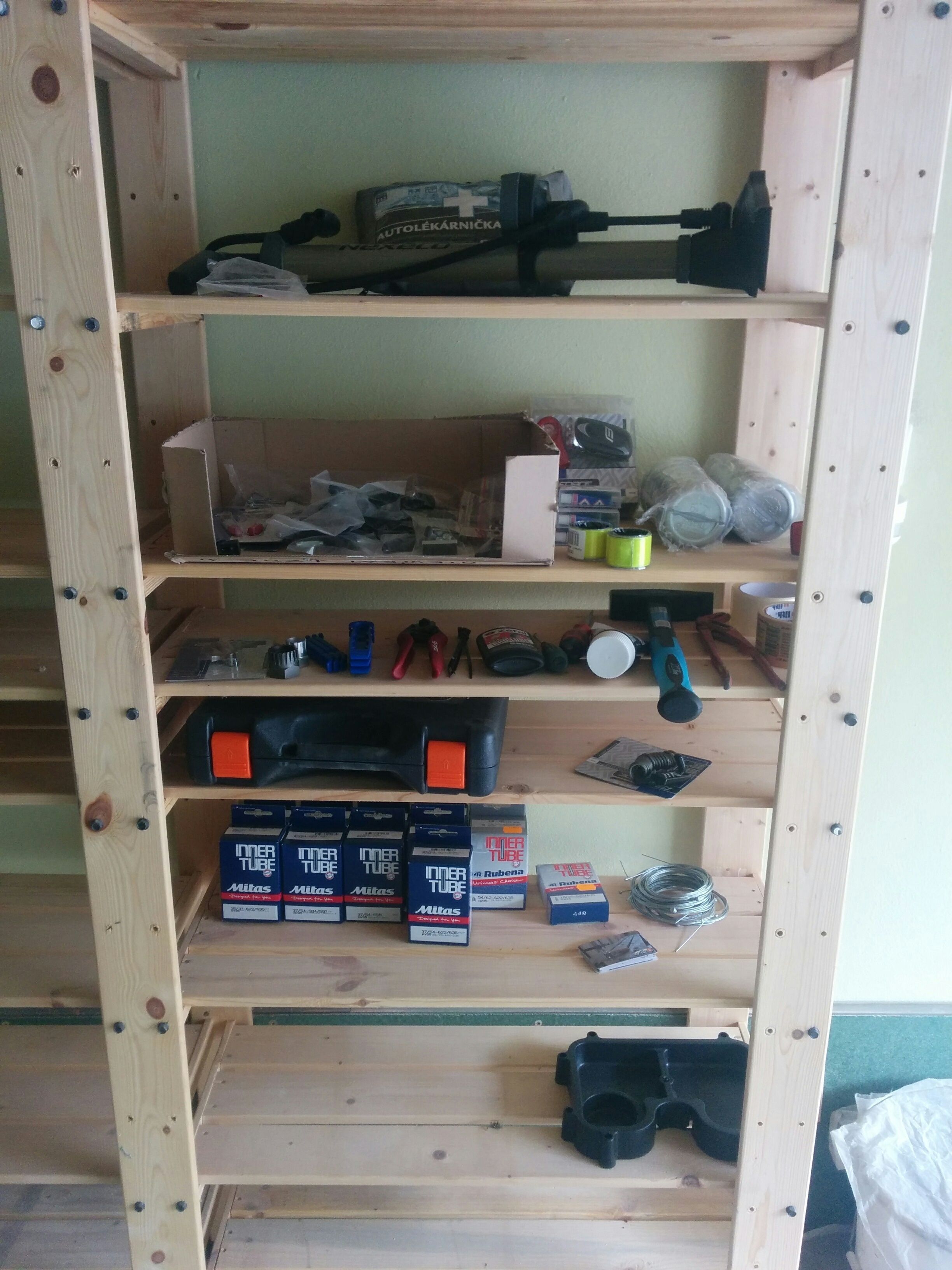 A wooden shelving unit with various tools and supplies, including boxes of Mitas lubricant and other items.