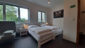 Une chambre avec deux lits, une chaise et deux tables de chevet avec des lampes. On peut voir des fenêtres et une porte.
