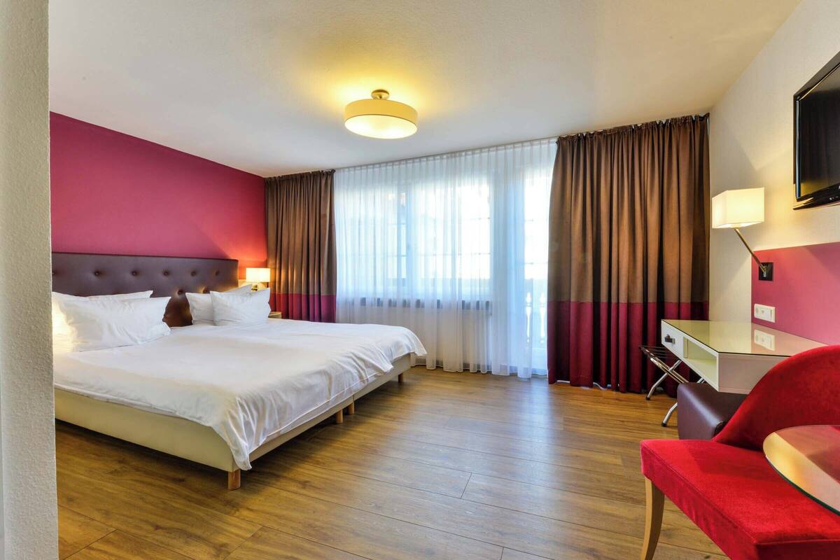 Habitación de hotel con una cama grande, un escritorio, una silla y un televisor en la pared.