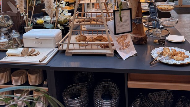 Un buffet de petit-déjeuner avec du pain, des viennoiseries et un panneau indiquant le menu.