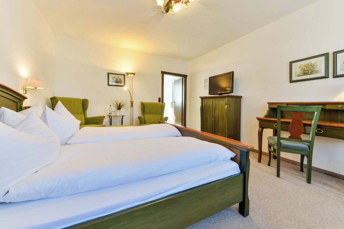 Habitación de hotel con cama doble, dos sillones verdes, escritorio con televisor y armario.