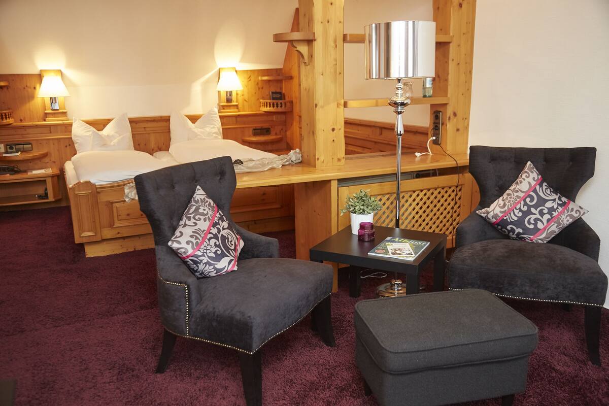 Habitación de hotel con dos camas, una zona de estar con sillones y una mesa, y detalles de madera.