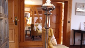 Une pièce avec un miroir reflétant un intérieur en bois, une chaise, une table avec un pot de plante et une lampe.
