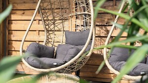 Une chaise en osier avec des coussins gris, placée contre un mur en bois.