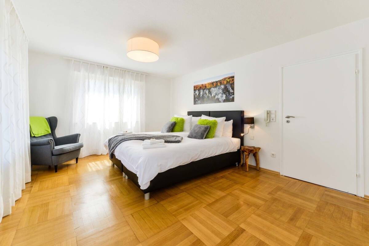 Un dormitorio moderno con una cama grande, una silla, una mesita de noche y un cuadro en la pared.