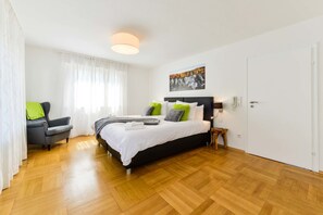 Een moderne slaapkamer met een groot bed, een stoel, een nachtkastje en een schilderij aan de muur.