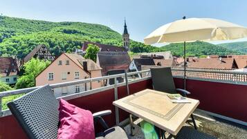 A balcony with a table, chairs, and an umbrella. The balcony overlooks a town with traditional buildings and a church tower.