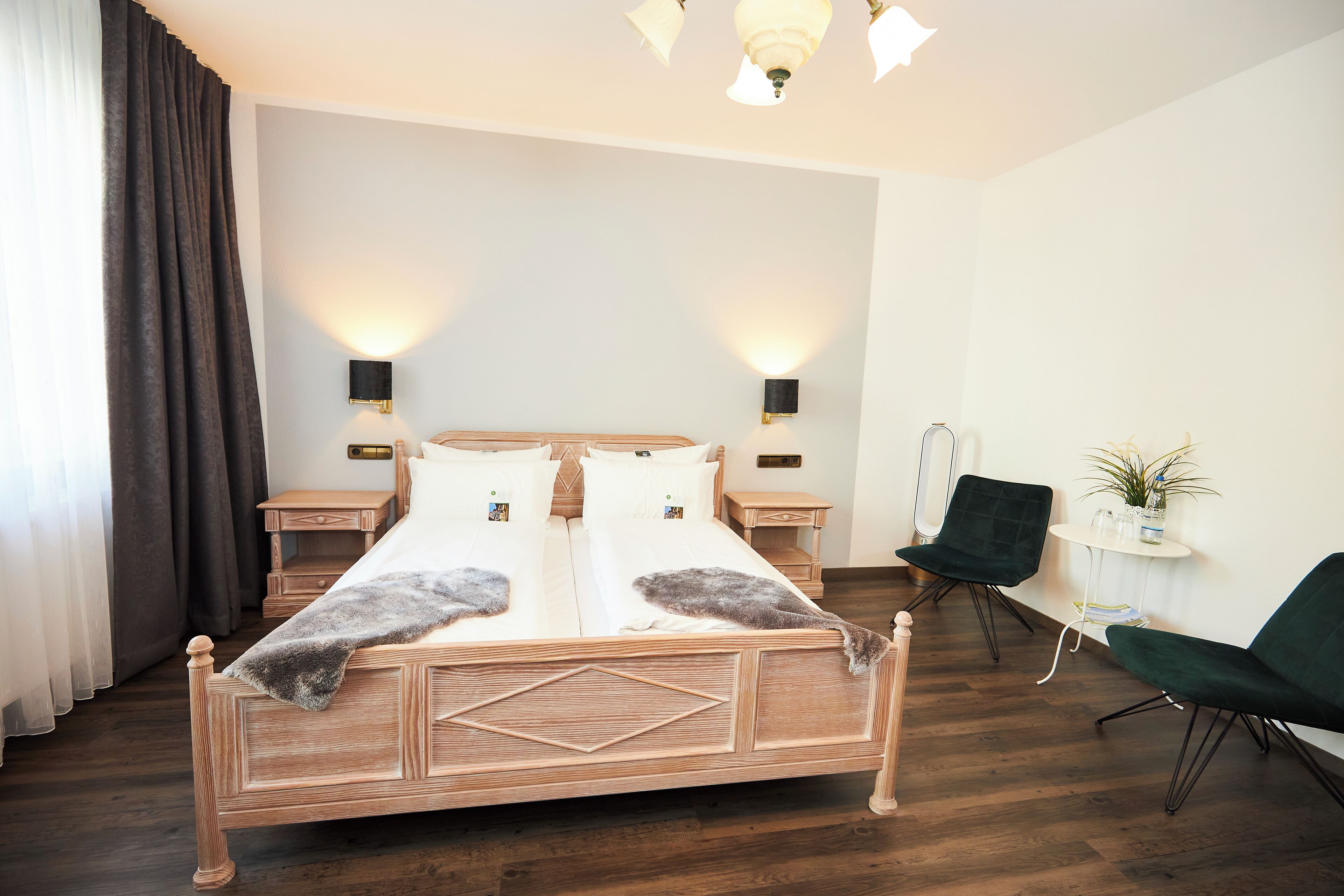 A modern bedroom with a wooden bed, two bedside tables, a nightstand, a green chair, and a small table with a plant.