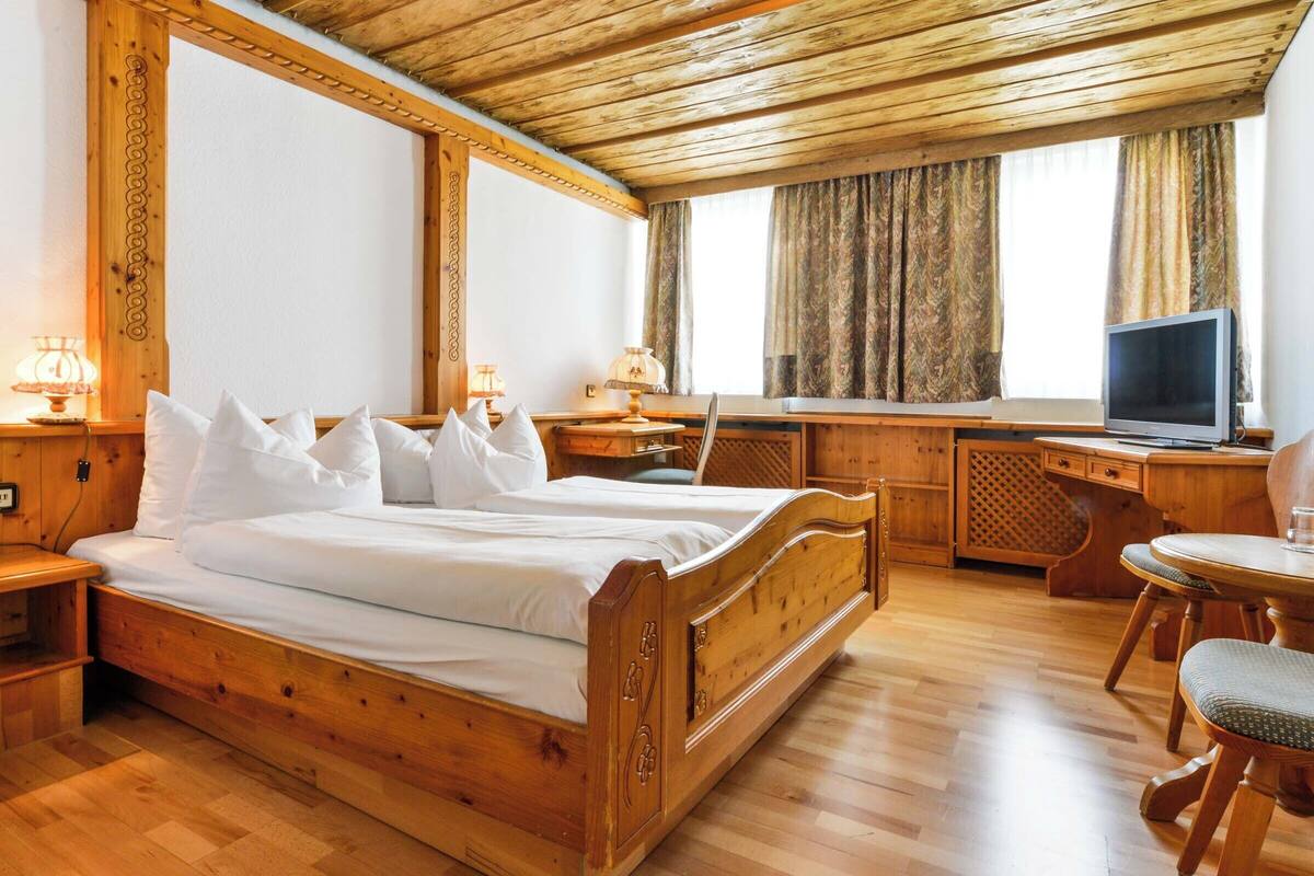 Un dormitorio de madera con cama, mesitas de noche, un escritorio y un televisor.