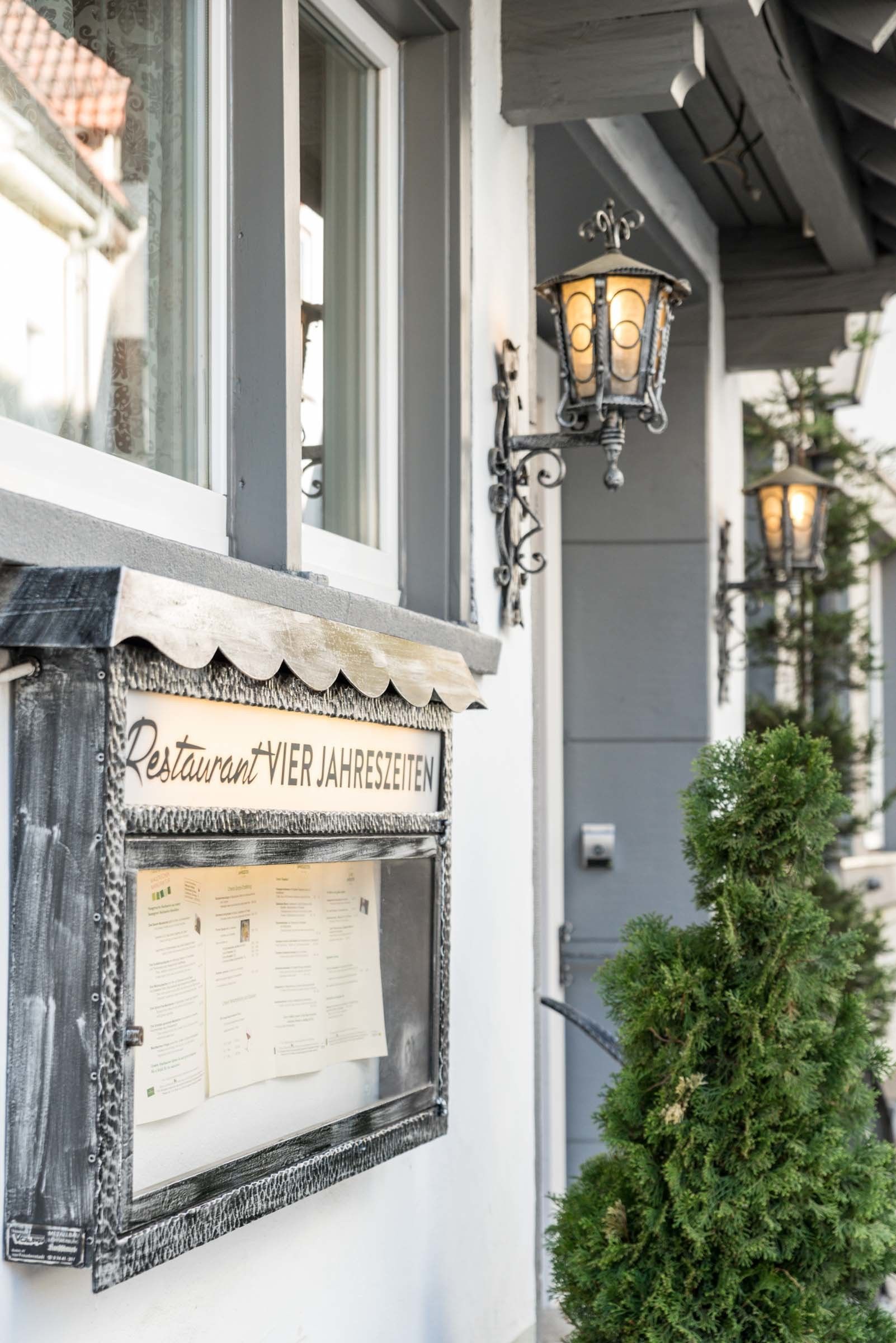 A restaurant sign with a menu board, outdoor lighting fixtures, and a small tree.