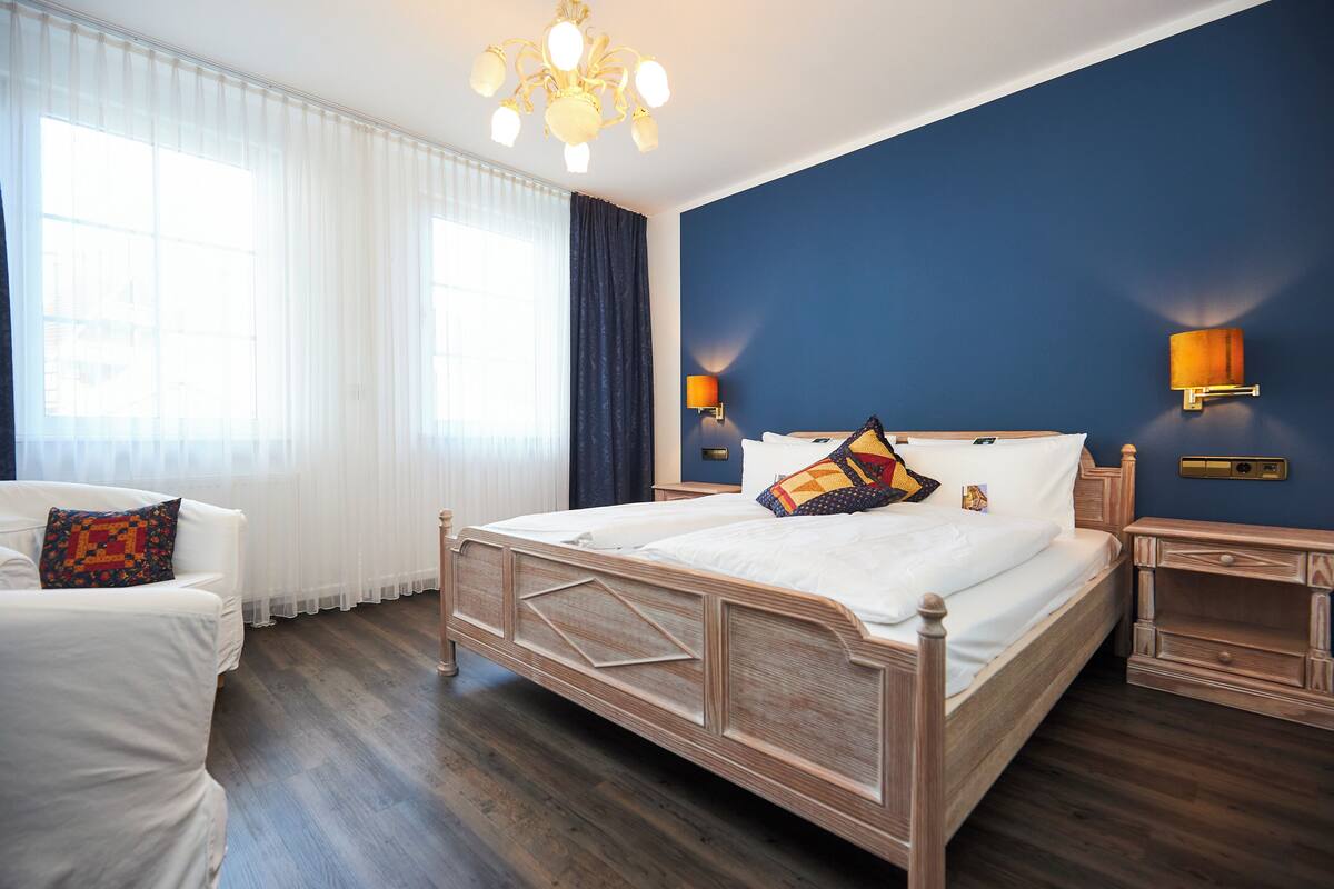Un dormitorio con cama de madera, cortinas blancas, una araña y dos lámparas de pared.