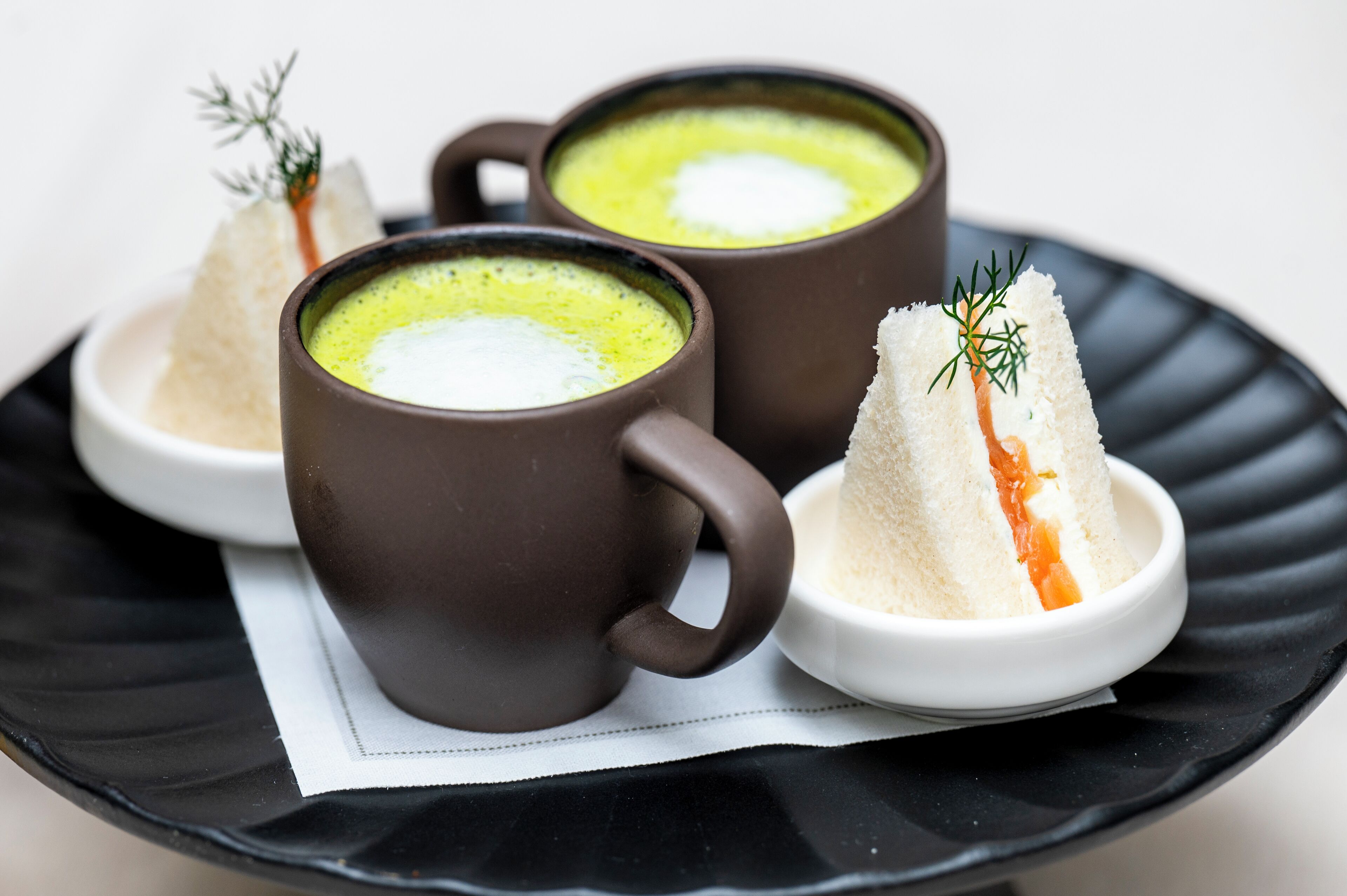 Duas canecas marrons com sopa verde e uma tigela branca com uma substância branca e uma fatia de salmão.