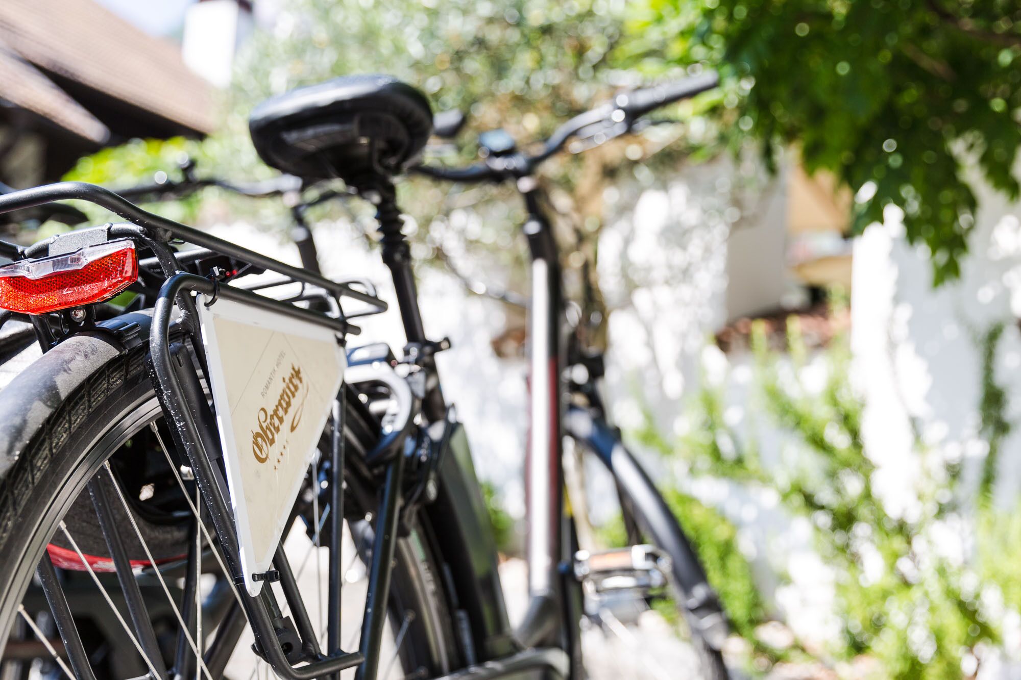 A bicycle with a white frame and a red tail light, parked outdoors.