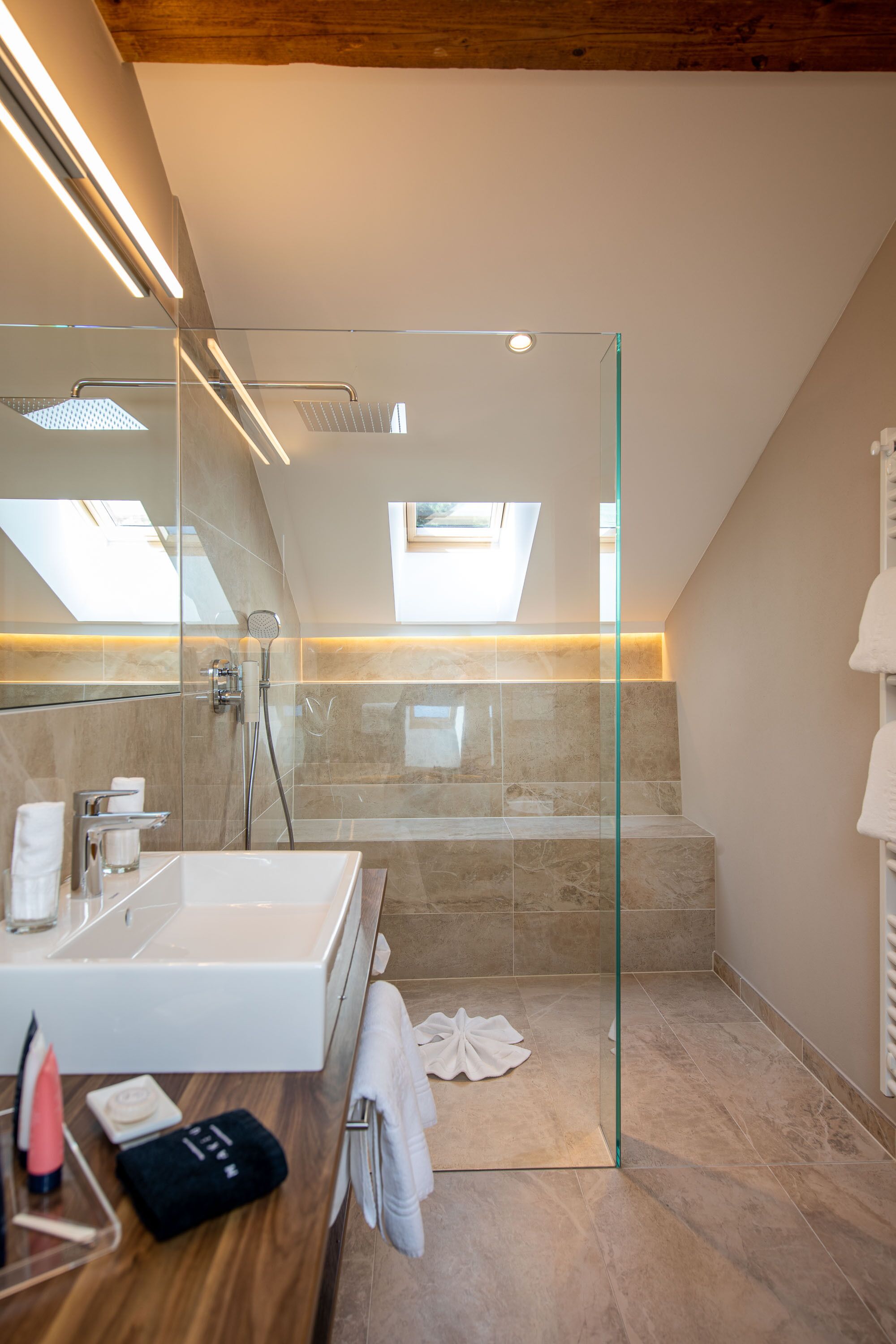 Un baño moderno con ducha de vidrio, un espejo grande y un tragaluz.