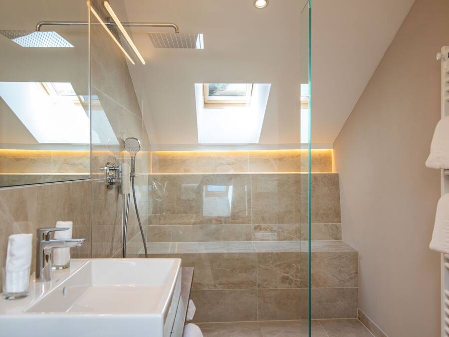 Un baño moderno con ducha de vidrio, un espejo grande y un tragaluz.