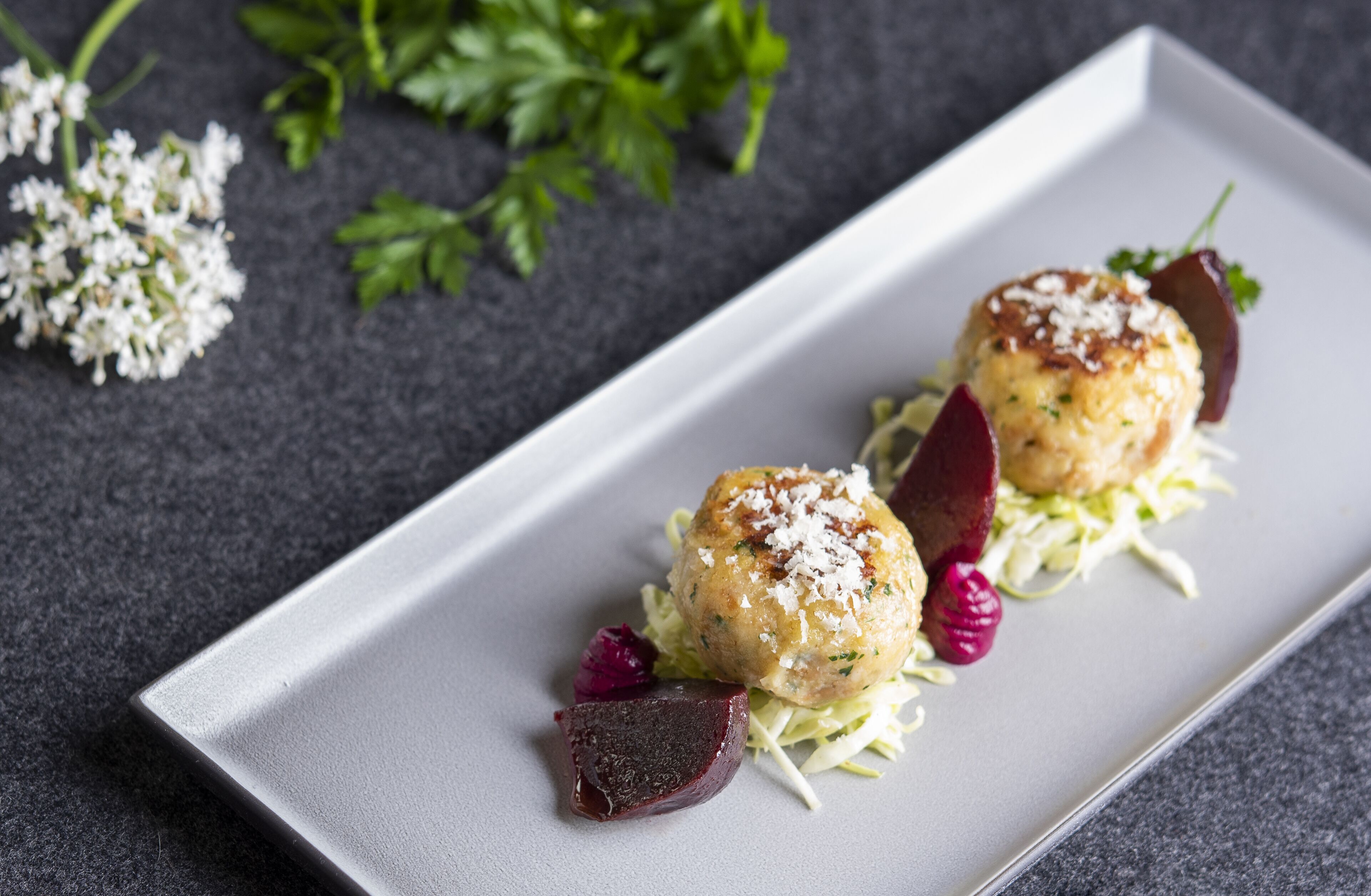 A rectangular plate with two round food items, garnished with herbs and a small piece of cheese, accompanied by a beet slice and shredded lettuce.