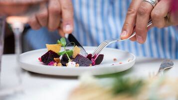 A person holding a fork with a plate of food, including beets and greens, on a table.